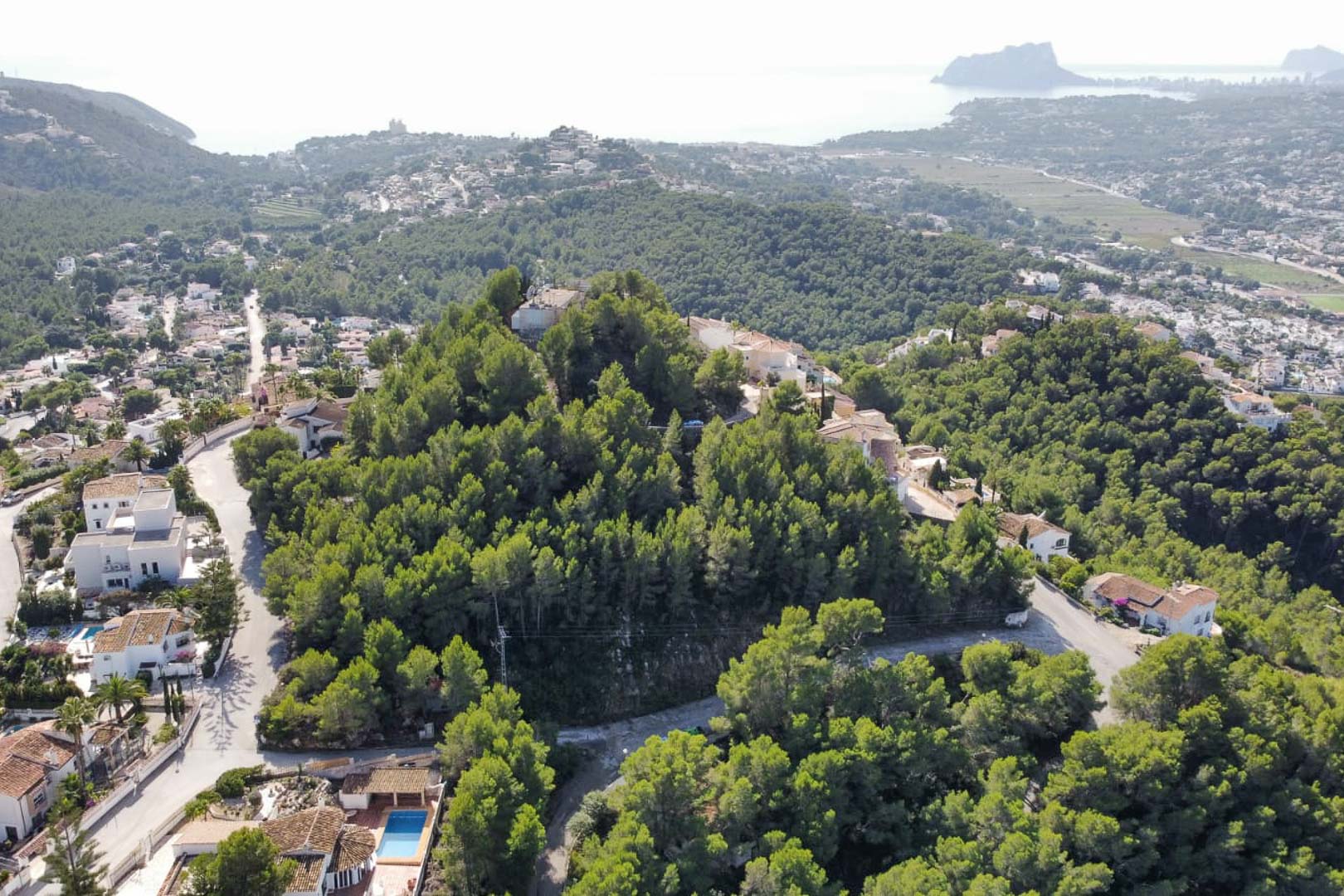 Vista aérea de la colina boscosa en Paichi, Moraira, destacando la parcela entre pinos con el Peñón de Ifach y el Mediterráneo al fondo.