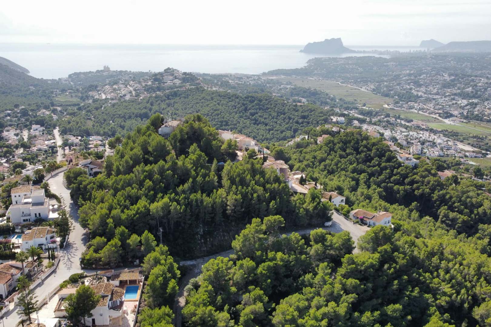 Vista aérea de la zona residencial de Paichi en Moraira, destacando la densa vegetación de pinos y las vistas panorámicas hacia el mar Mediterráneo y el Peñón de Ifach.