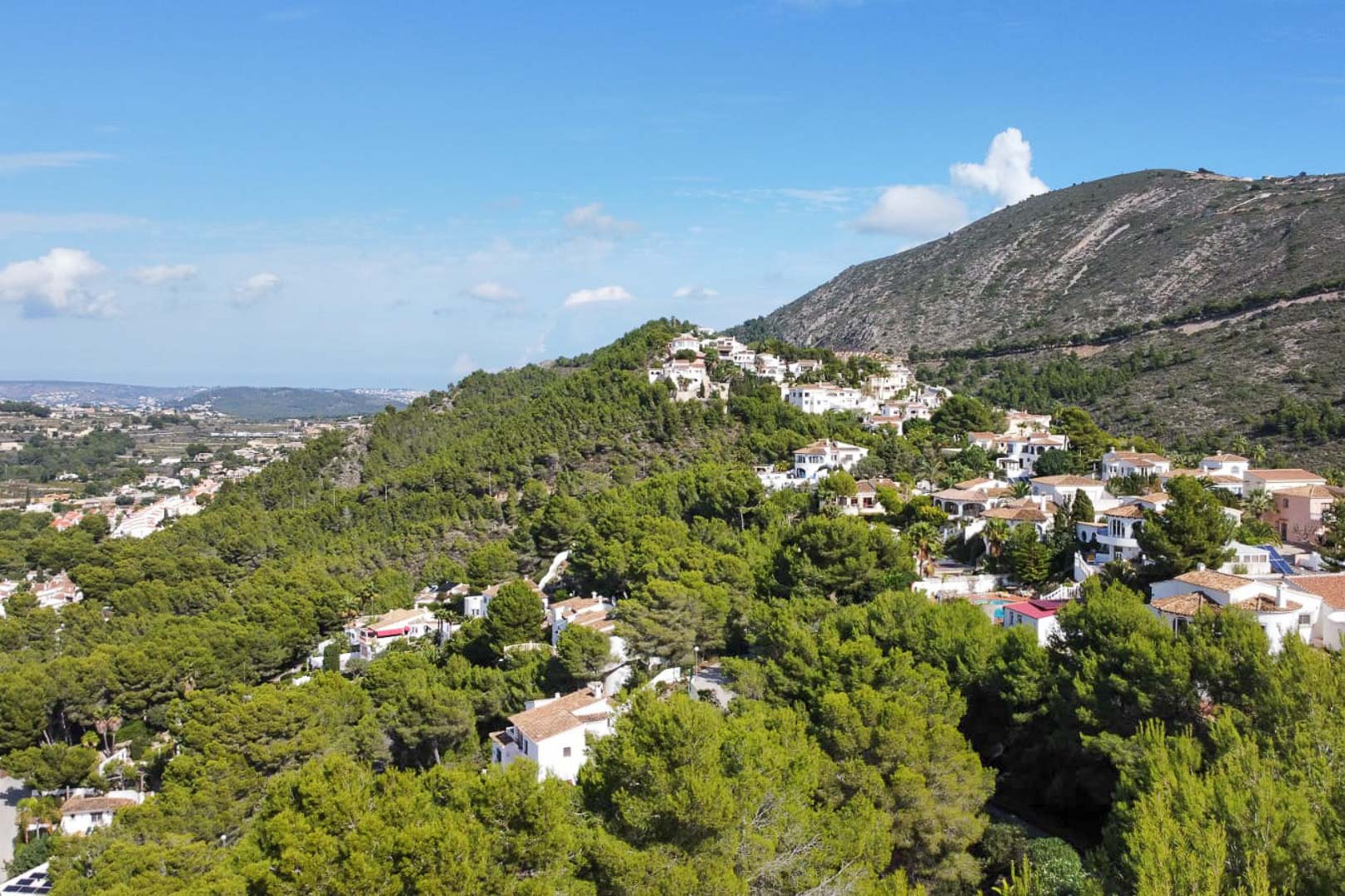 Vista aérea de la zona residencial de Paichi en Moraira, destacando la integración de villas blancas entre densos pinares y amplias vistas a la montaña.