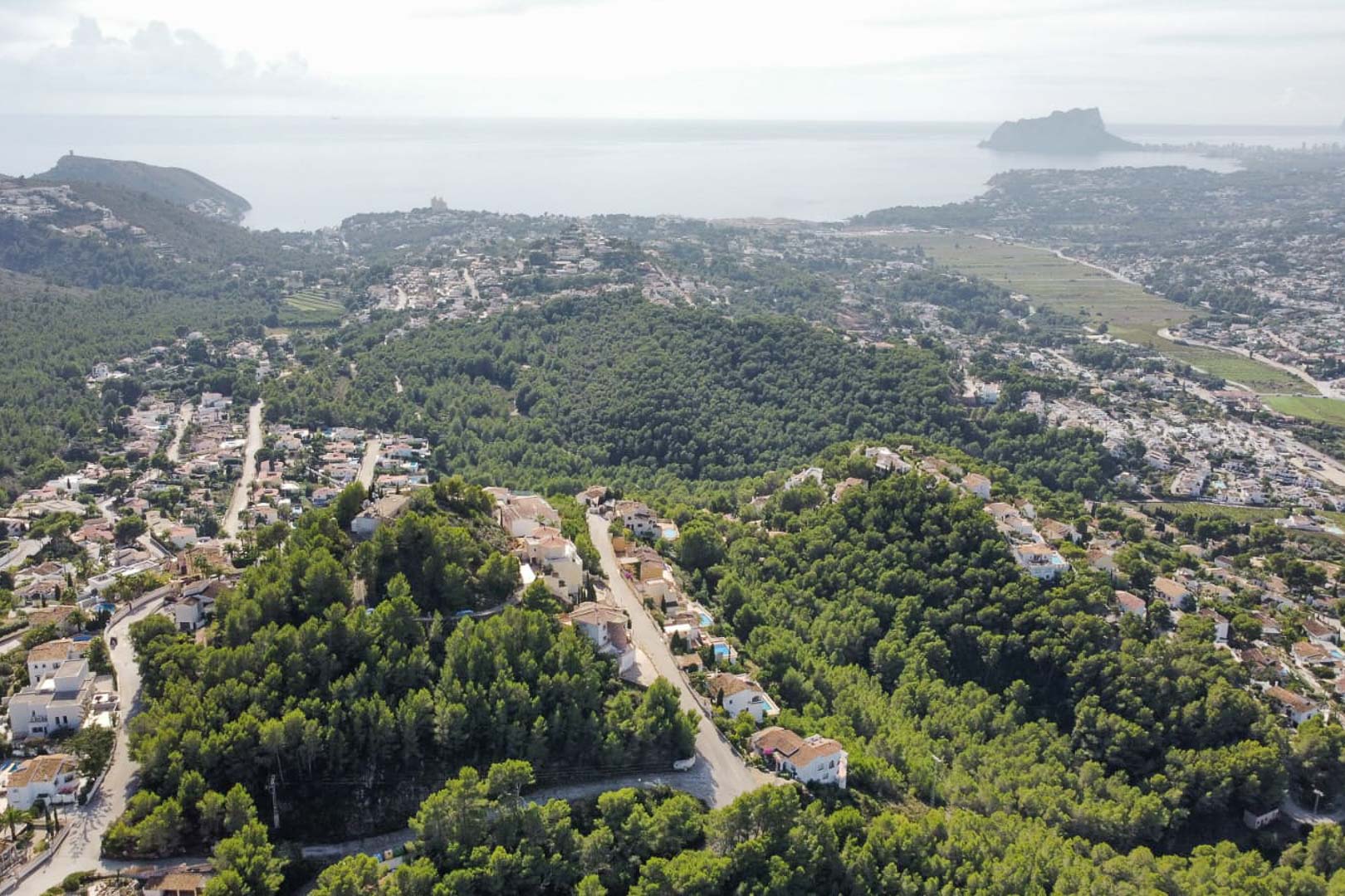 Vista aérea panorámica de la zona residencial de Paichi, mostrando la densa vegetación de pinos, villas unifamiliares y el Peñón de Ifach al fondo sobre el mar Mediterráneo.