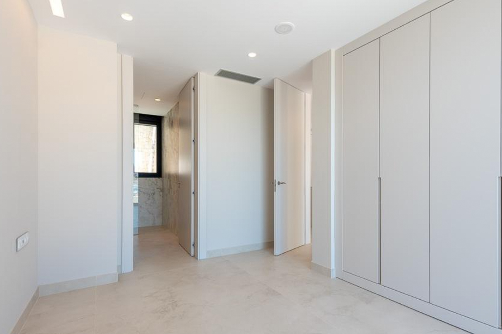 Dormitorio con armarios empotrados de suelo a techo, iluminación LED integrada y acceso a un baño en suite con elegantes acabados de mármol.