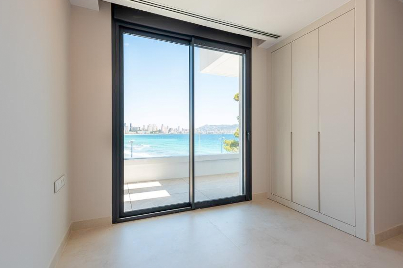 Dormitorio con armarios empotrados de suelo a techo y ventanal corredero con vistas directas al mar y al perfil urbano de Benidorm.
