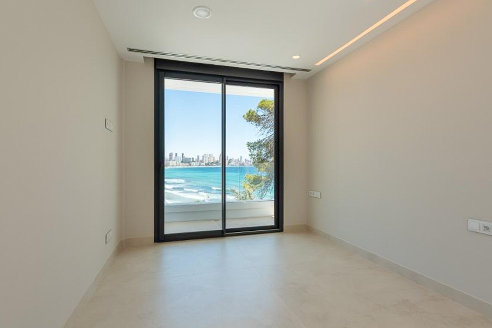Dormitorio u oficina con suelo porcelánico claro, iluminación LED integrada y acceso directo a terraza con vistas panorámicas al mar y Benidorm.