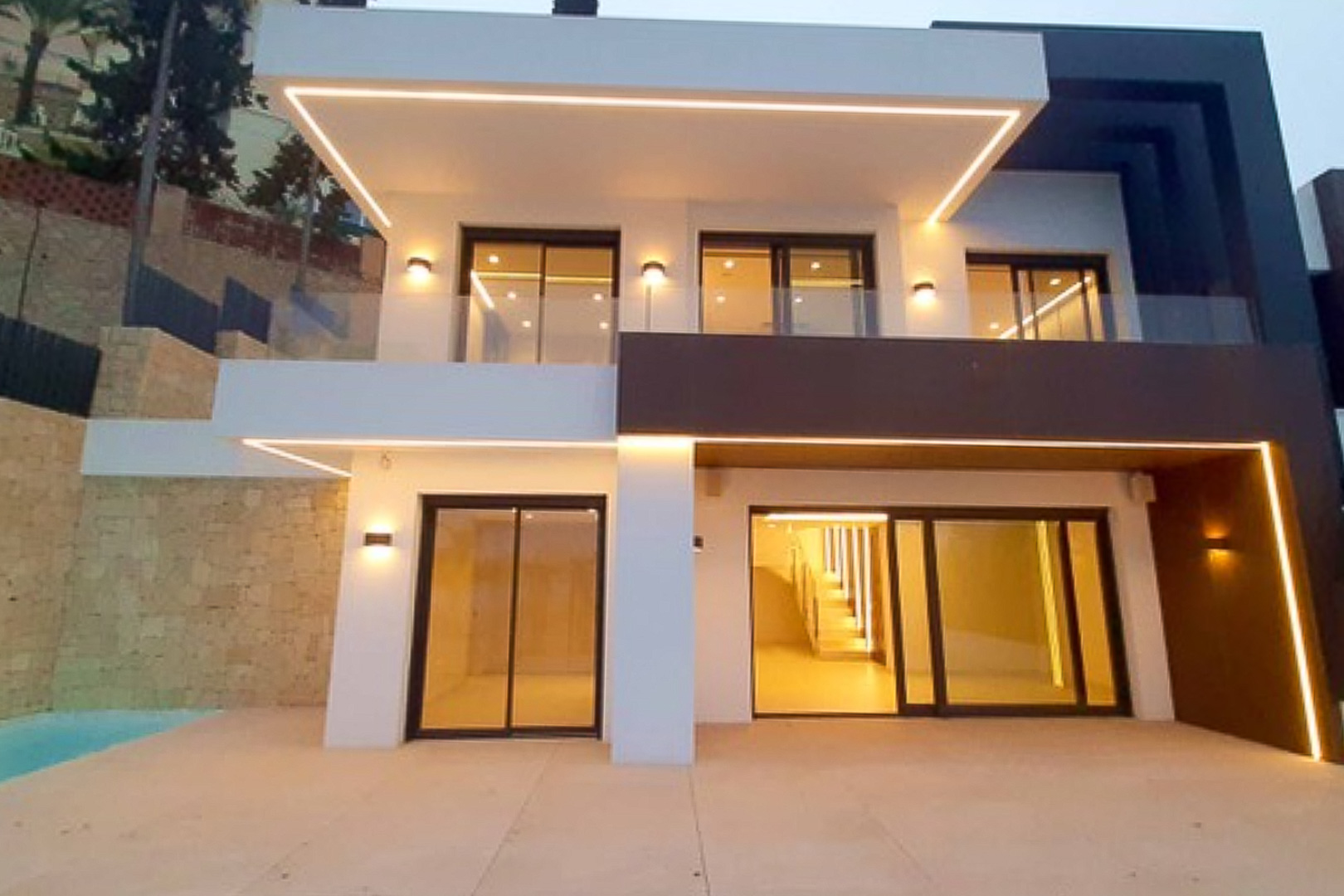 Fachada moderna con iluminación LED integrada en voladizos, grandes ventanales correderos y terrazas con barandillas de cristal en un diseño de volúmenes contrastados.