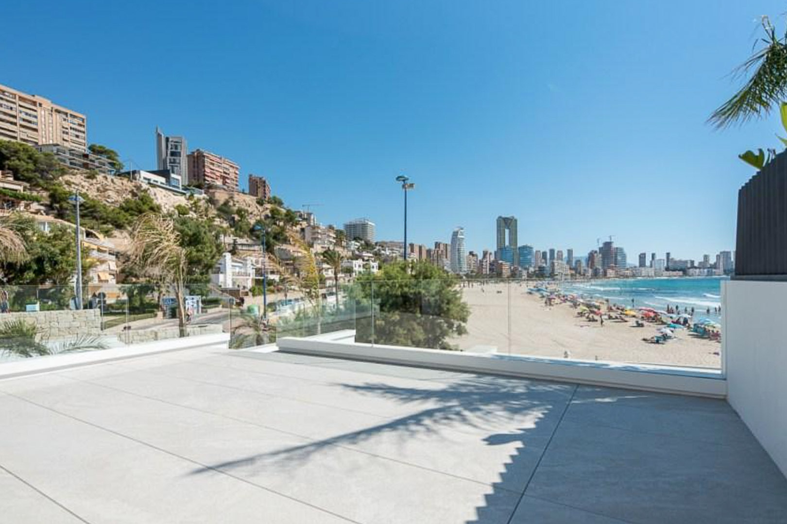 Terraza exterior con suelo de gres de gran formato y barandilla de cristal, ofreciendo vistas panorámicas a la playa y al perfil urbano de Benidorm.