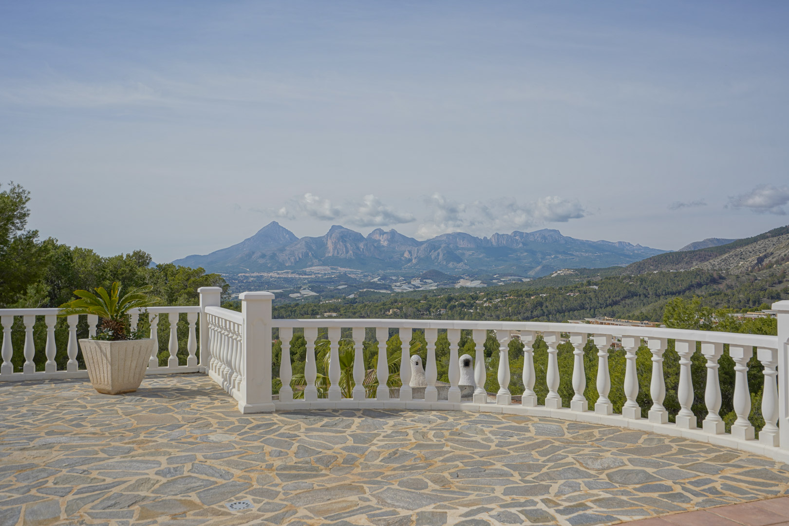 Terraza con suelo de piedra natural y balaustrada blanca que ofrece vistas panorámicas a las montañas del Puig Campana y la Sierra Aitana.