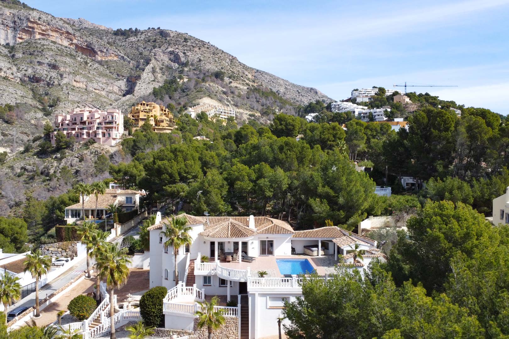 Vista aérea de la villa con tejados de teja, piscina privada y amplias terrazas blancas, rodeada de pinos y bajo la majestuosa Sierra de Bernia.