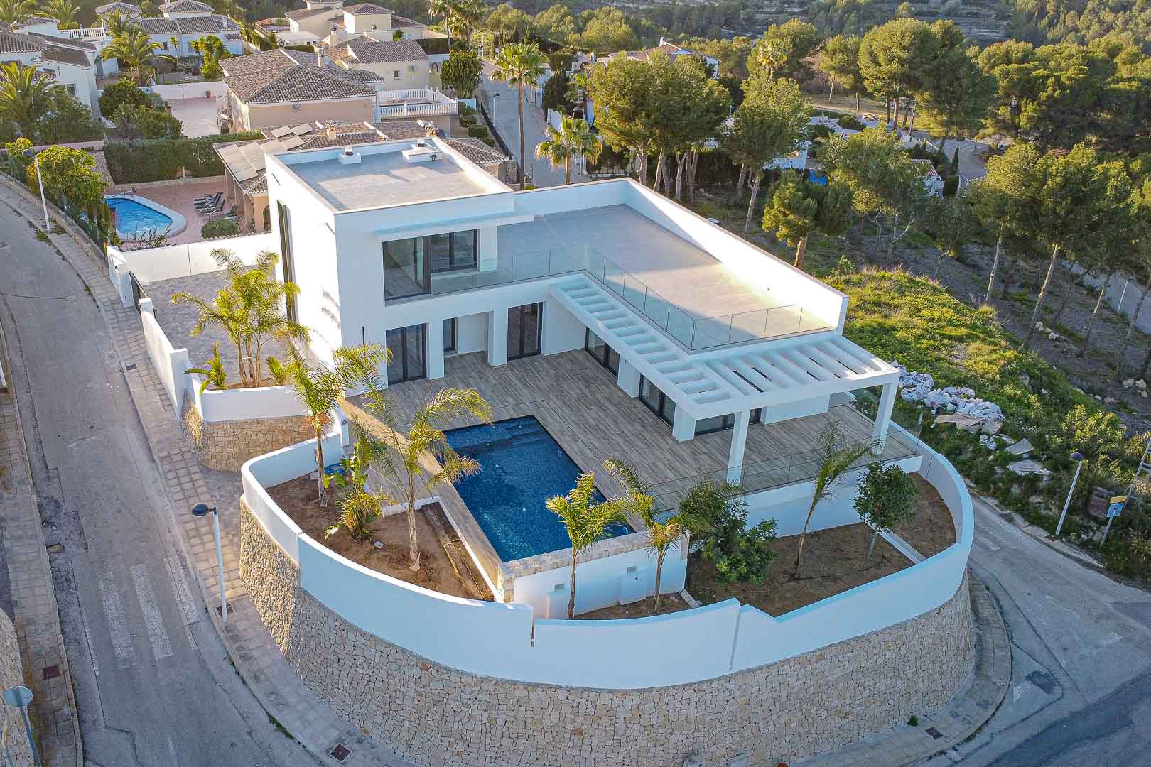 Vista aérea de villa moderna con piscina azul, terraza de madera y jardín mediterráneo en Benimeit, Moraira.