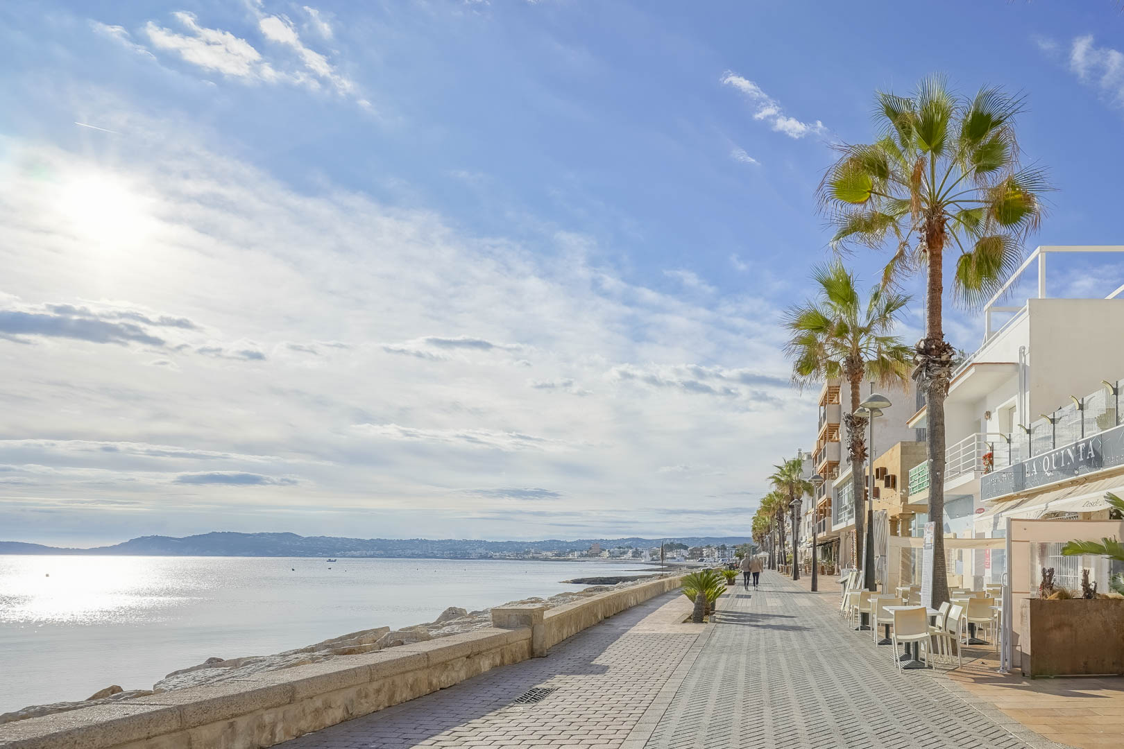 Paseo marítimo de Jávea con palmeras y vistas al Mediterráneo, ubicado cerca de la villa. La costa muestra aguas tranquilas bajo un cielo despejado.