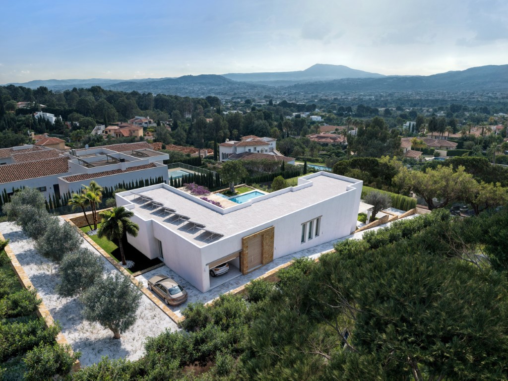 Vista aérea de la villa moderna con paneles solares, garaje integrado y jardín de olivos con amplias vistas al valle y las montañas de Jávea.