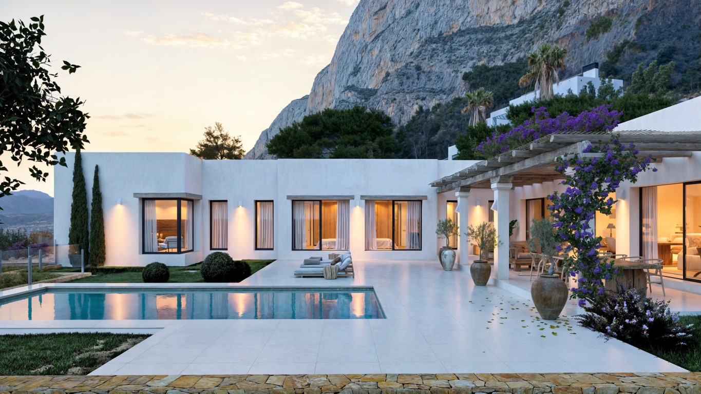 Vista exterior de la villa con piscina, terraza de gres porcelánico y pérgola de madera con buganvillas, bajo los impresionantes acantilados del Montgó al atardecer.