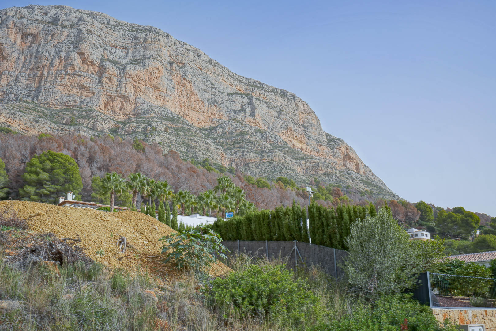 Vista panorámica de los imponentes acantilados del Montgó desde la parcela en construcción, rodeada de vegetación mediterránea y pinos.