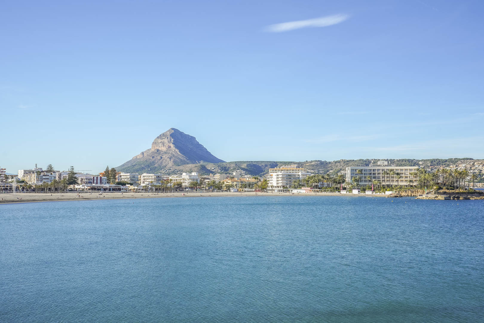 Vista panorámica de la bahía de Jávea con el emblemático Montgó al fondo, destacando la proximidad de la villa al mar y al centro urbano bajo un cielo despejado.