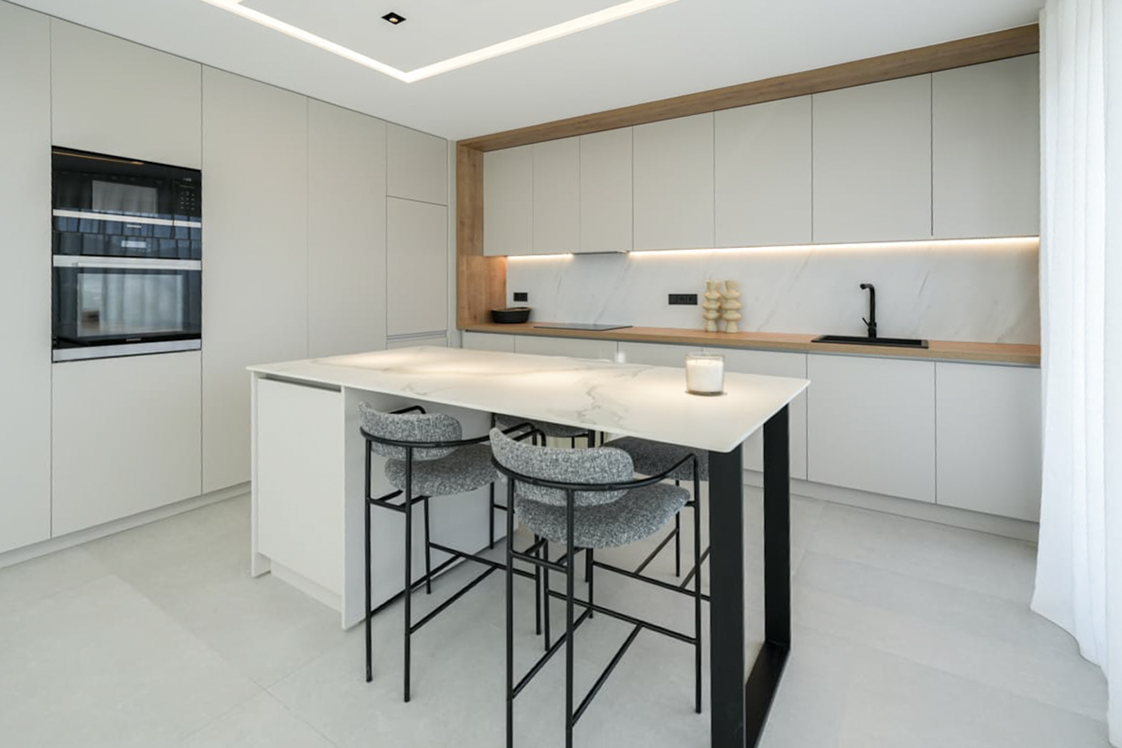 Detalle de la cocina con isla de mármol y taburetes grises. Diseño moderno y funcional.