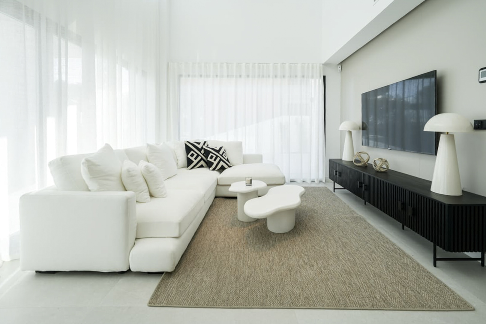 Salón luminoso con sofá blanco modular, mesa auxiliar moderna y alfombra de yute.