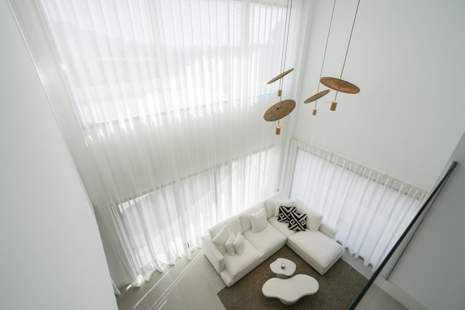 Vista elevada del salón con cortinas blancas, sofá modular y lámparas colgantes de diseño.