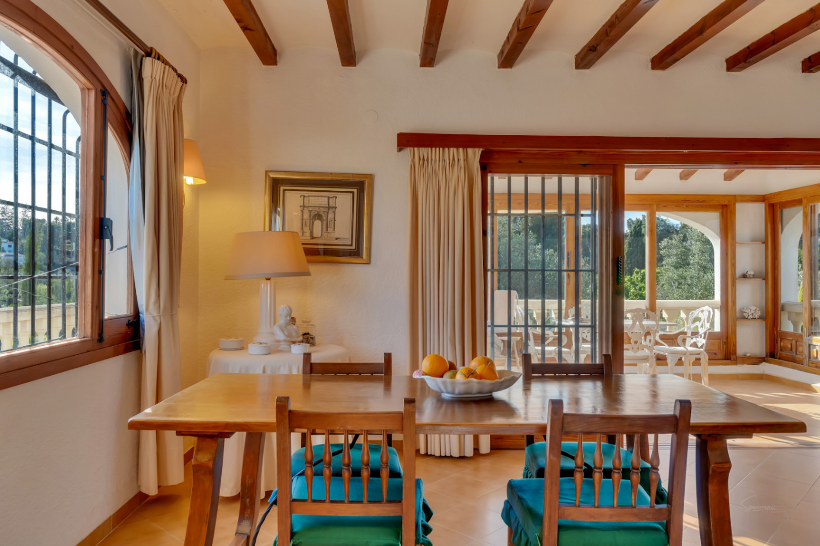 Comedor rústico con vigas de madera a la vista, mesa de madera maciza y acceso directo a una terraza acristalada con abundante luz natural.
