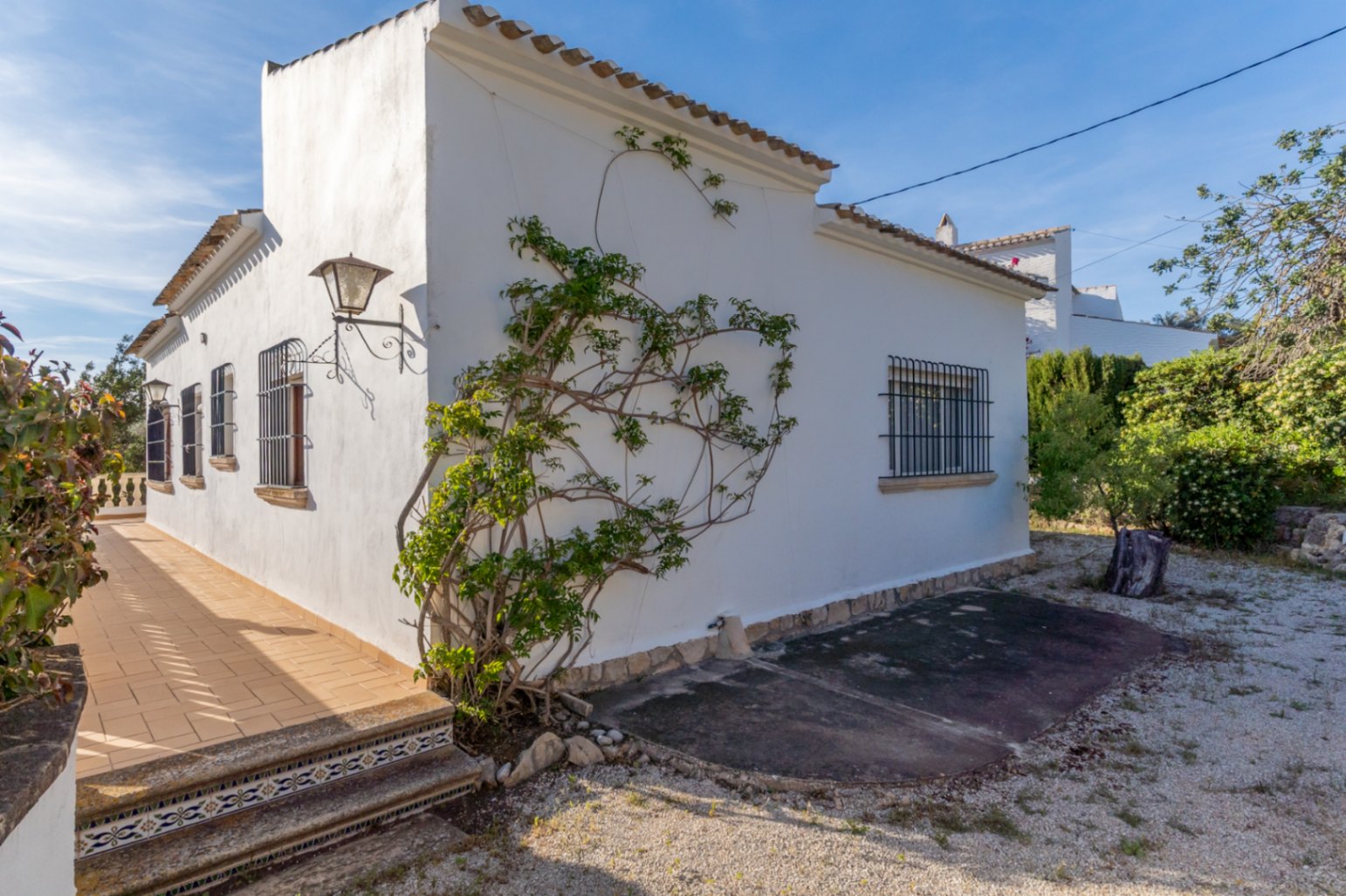 Exterior de la villa con fachada blanca, ventanas protegidas por rejas de hierro forjado y una terraza lateral con escalones de cerámica tradicional.