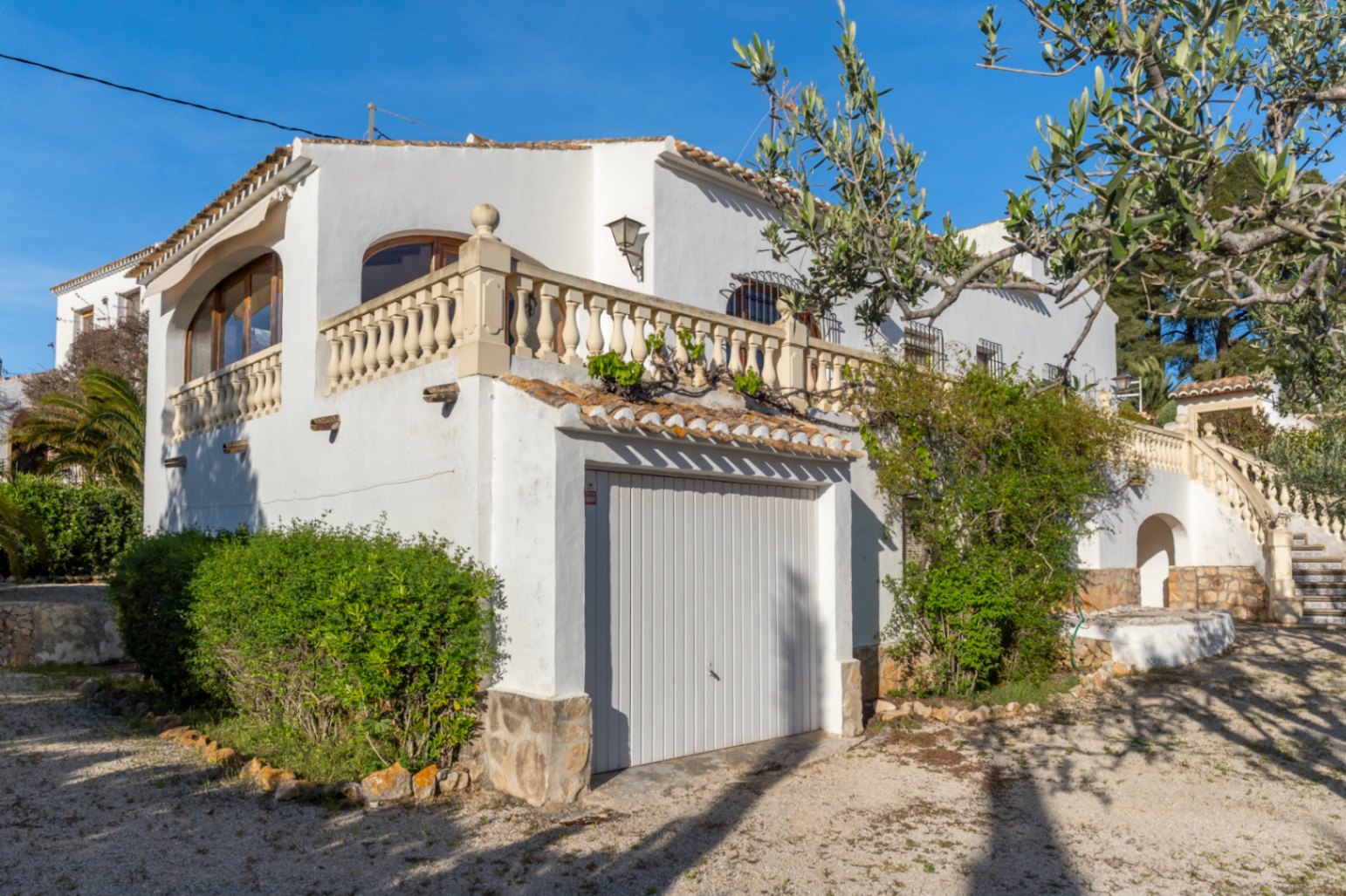 Fachada blanca de estilo mediterráneo con garaje integrado, balaustrada de piedra tradicional y escalinata exterior decorada con azulejos cerámicos.