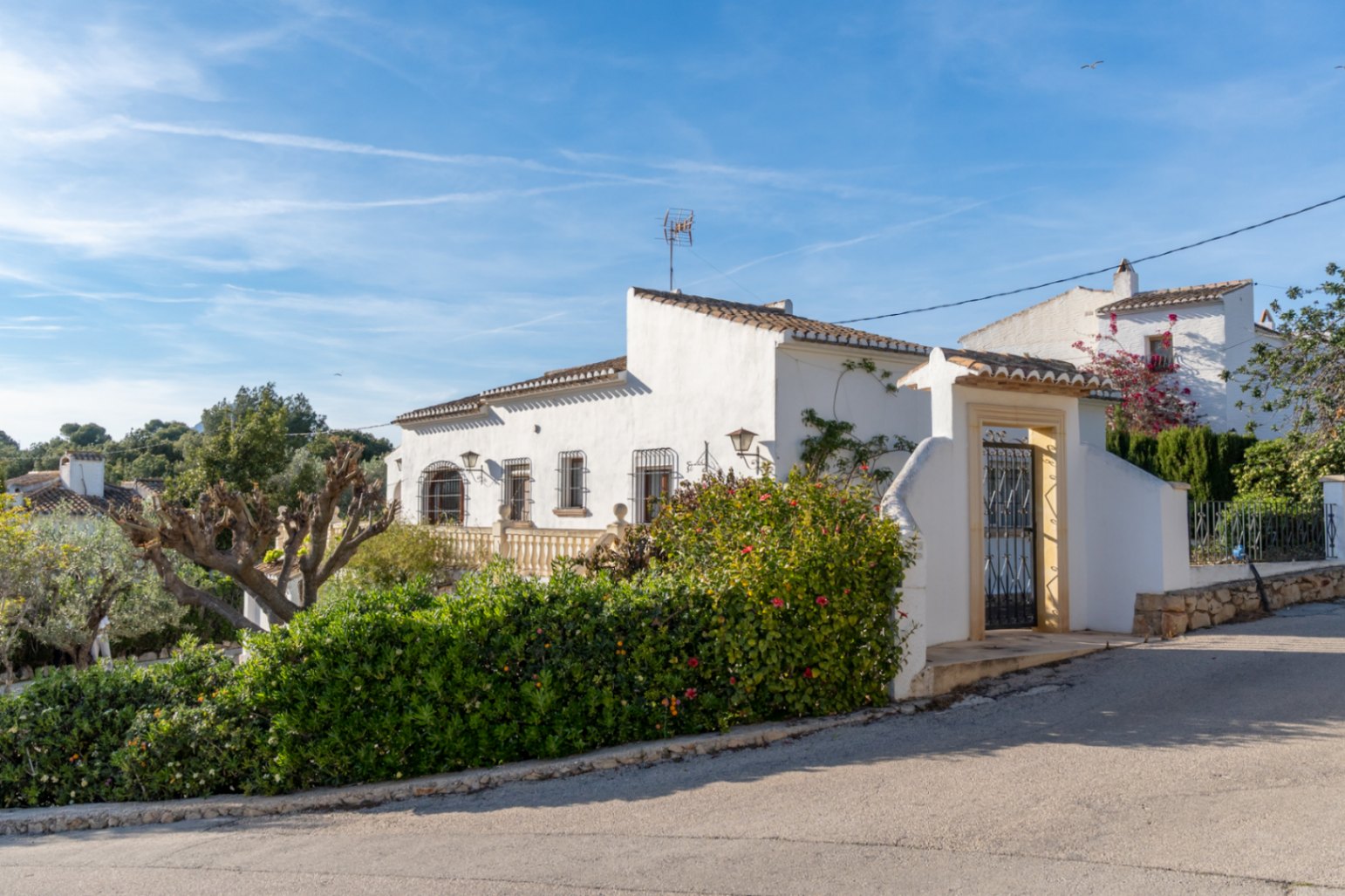 Fachada exterior de estilo mediterráneo con muros blancos, rejas de hierro forjado y un portal de entrada con marco de piedra tosca y tejadillo cerámico.