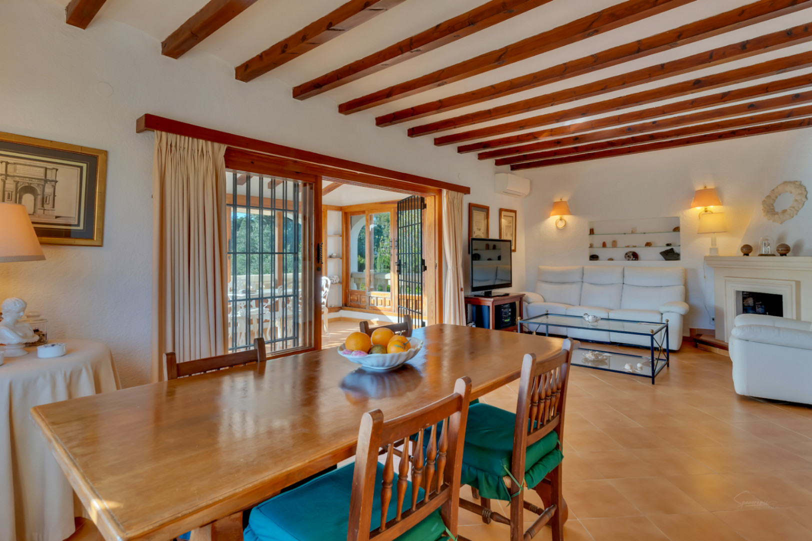 Salón-comedor luminoso con vigas de madera a la vista, suelos de gres y acceso directo a la terraza acristalada a través de amplios ventanales corredizos.