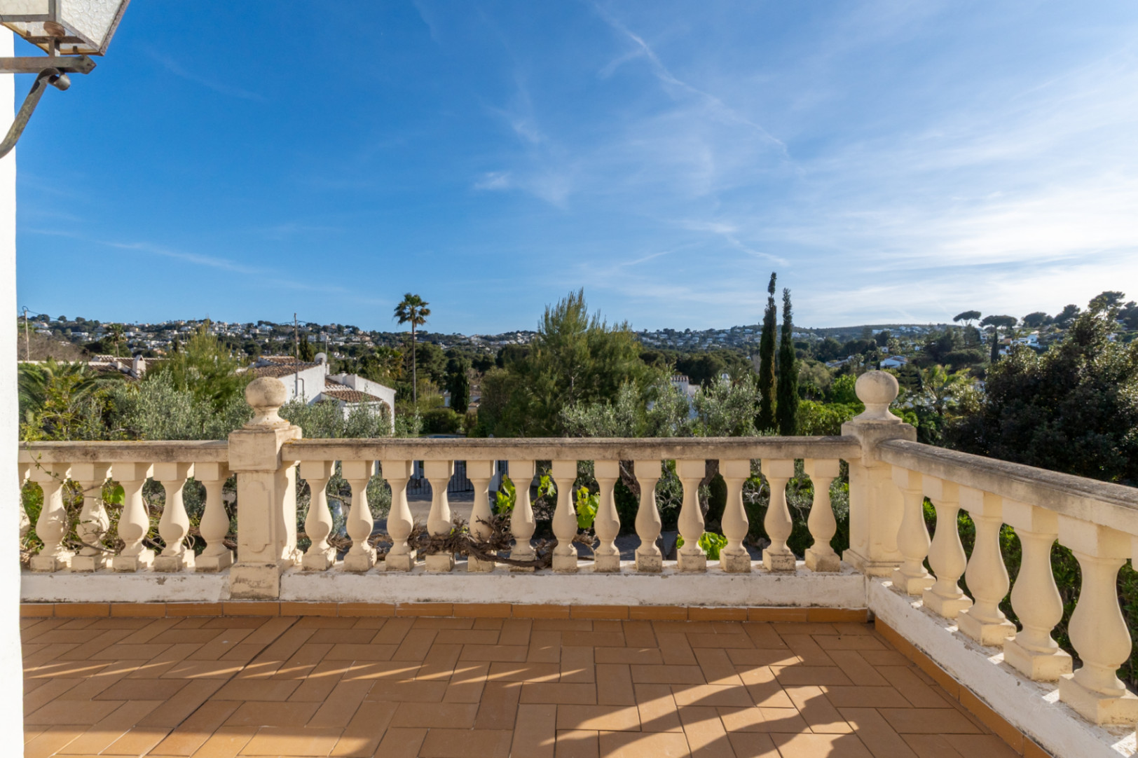 Terraza elevada con suelo de baldosas de barro y balaustrada clásica, ofreciendo vistas despejadas al entorno verde y residencial de Cap Martí en Jávea.