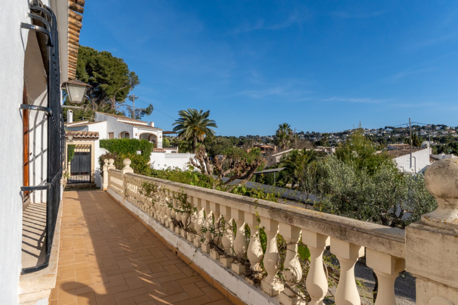 Terraza exterior con suelo de baldosas de barro y balaustrada clásica, ofreciendo vistas despejadas al entorno residencial de Cap Martí en Jávea.
