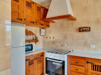 Cocina con mobiliario de madera rústica, electrodomésticos blancos y paredes alicatadas en tonos crema.