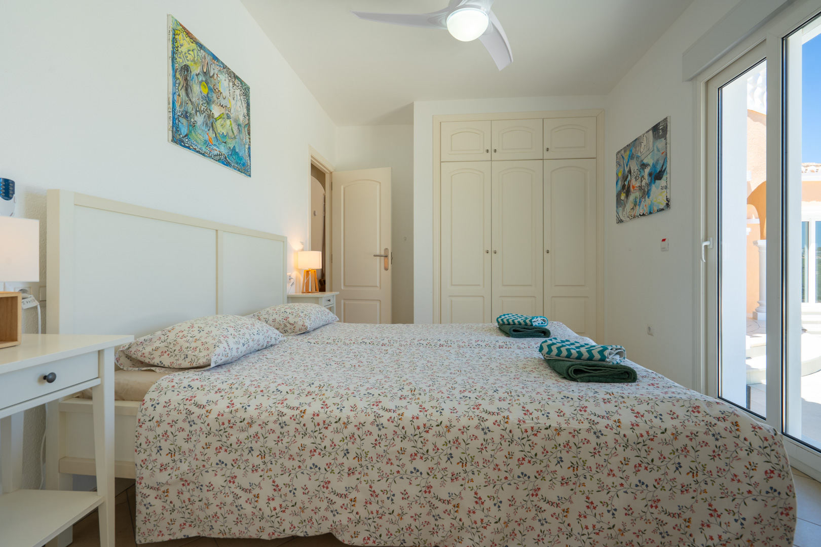 Dormitorio luminoso con armarios empotrados, ventilador de techo y acceso directo al exterior mediante puertas de PVC de doble acristalamiento.