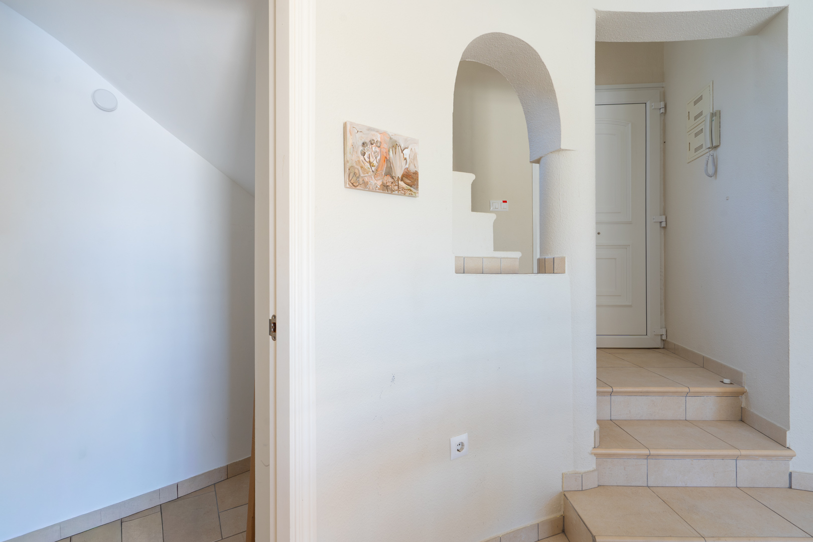 Hall de entrada con escalera interior, suelos cerámicos en tonos neutros y un arco decorativo que aporta carácter mediterráneo al espacio.