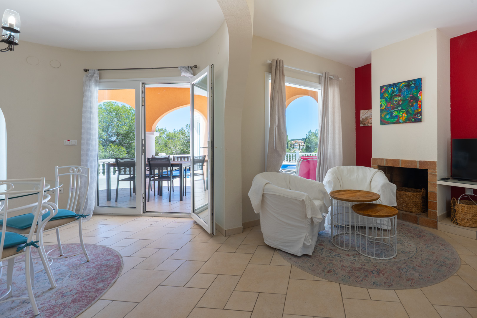 Salón comedor de concepto abierto con chimenea de obra, suelos cerámicos y acceso directo a la terraza cubierta mediante ventanales de PVC con doble acristalamiento.