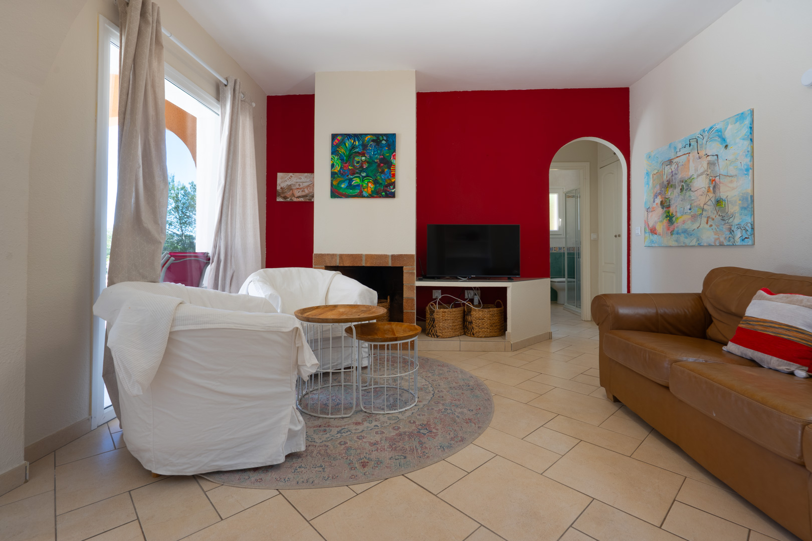 Salón con pared de acento roja, chimenea integrada y paso arqueado. Dispone de suelos cerámicos, mobiliario de cuero y gran entrada de luz natural.