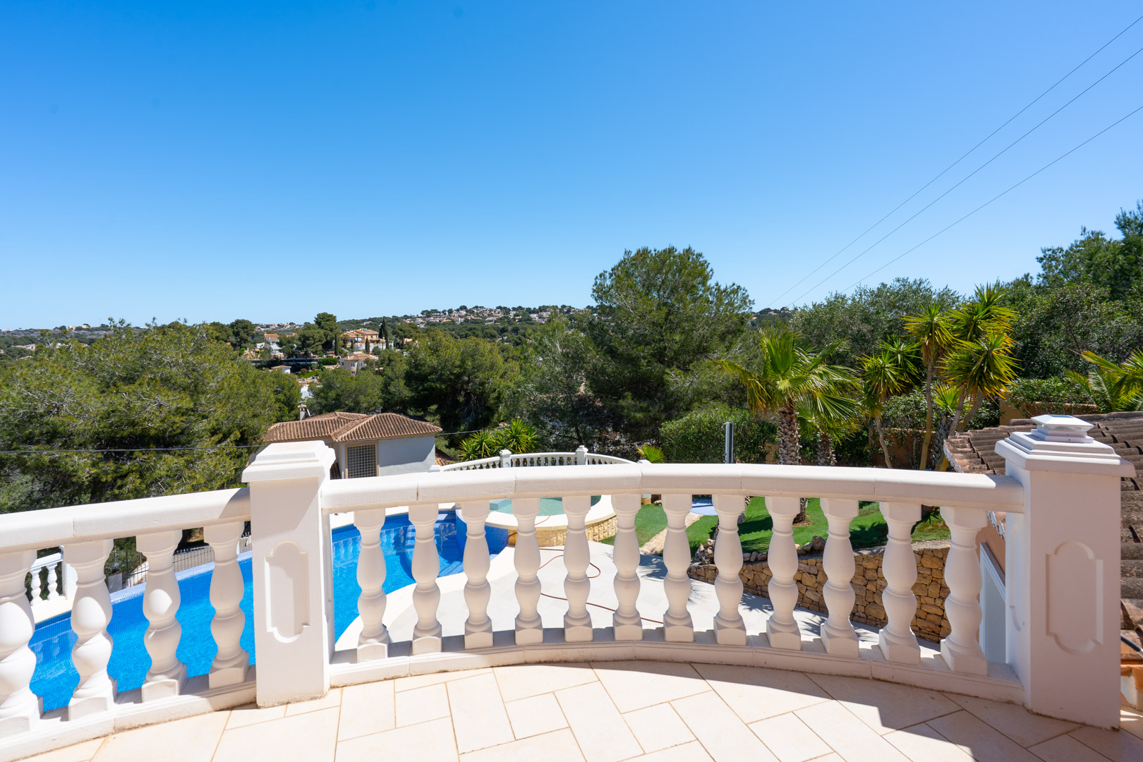 Terraza superior con balaustrada blanca clásica que ofrece vistas despejadas a la piscina, el jardín mediterráneo y las colinas circundantes de Jávea.