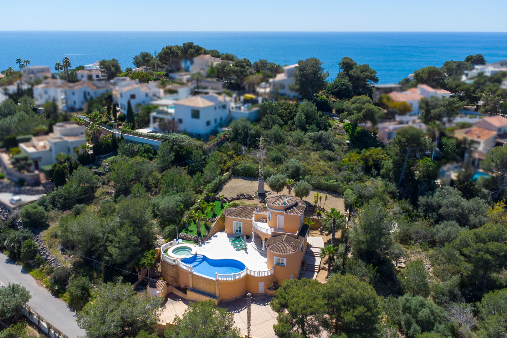 Vista aérea de la villa con fachada color tierra, destacando su piscina de diseño curvo, terrazas con balaustradas blancas y vistas panorámicas al mar Mediterráneo.