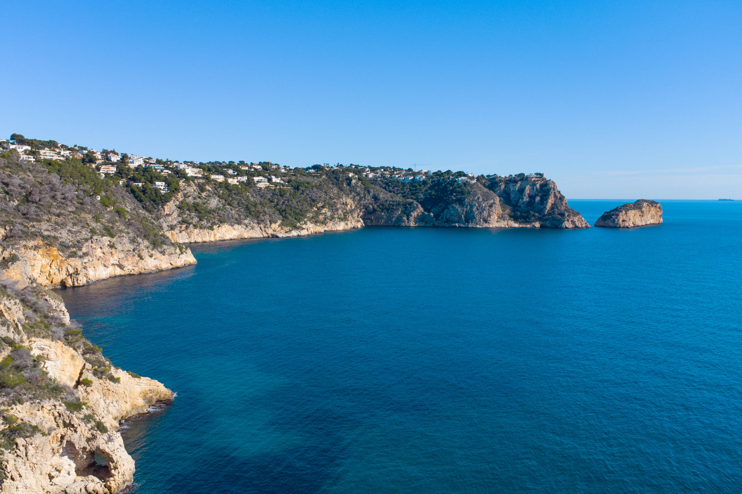 Vista panorámica de los acantilados de Jávea y el mar Mediterráneo, mostrando la escarpada costa rocosa y las zonas residenciales situadas frente al litoral.