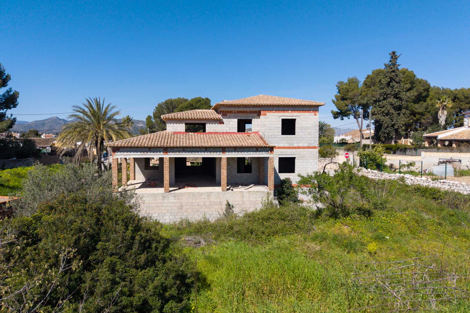 Estructura de vivienda unifamiliar en dos niveles con tejado de teja cerámica, amplios porches sostenidos por pilares de ladrillo y vistas despejadas al entorno natural.