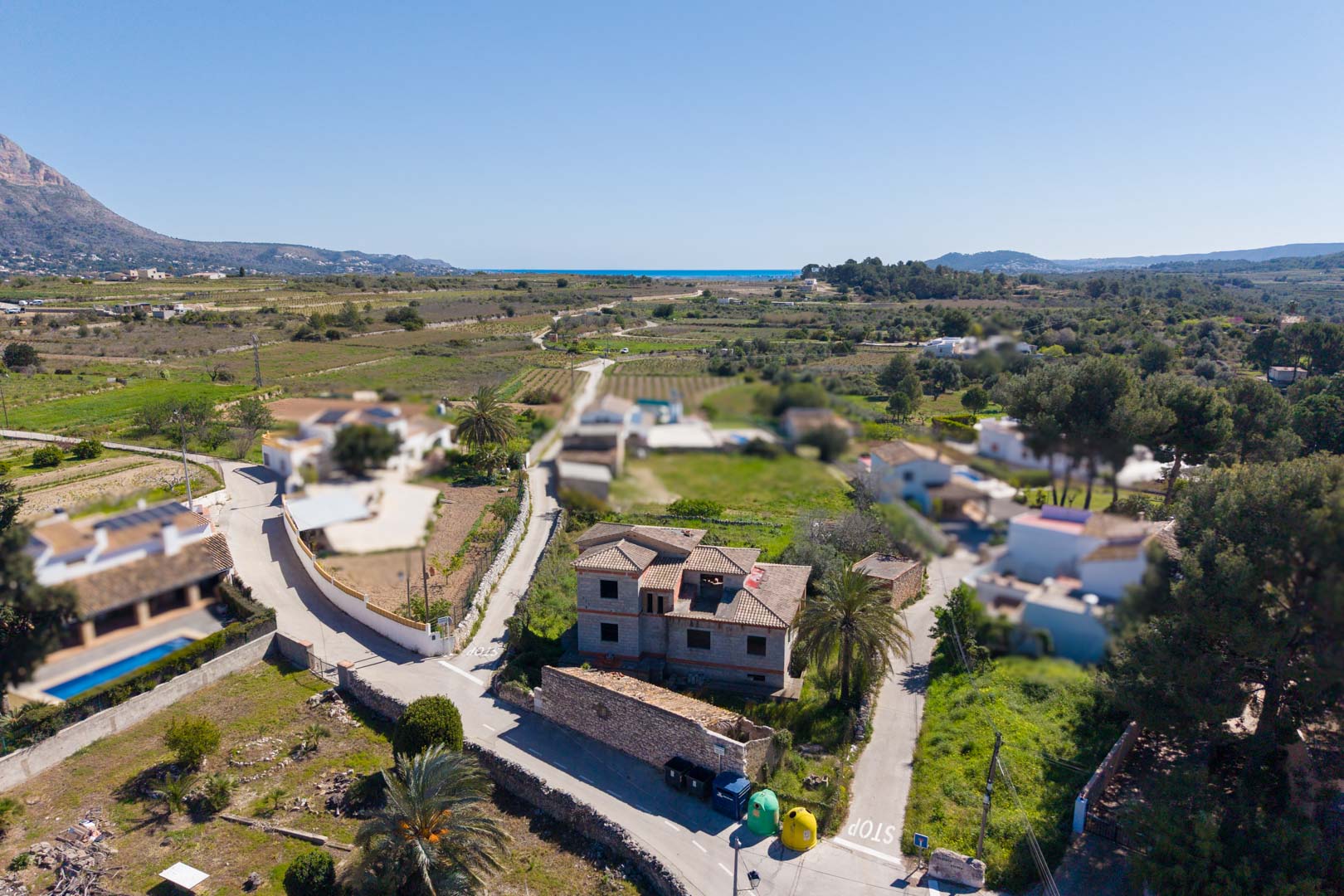 Vista aérea de la estructura de la vivienda con cubierta de teja, rodeada de terreno natural con vistas al Montgó y al mar Mediterráneo en el horizonte.