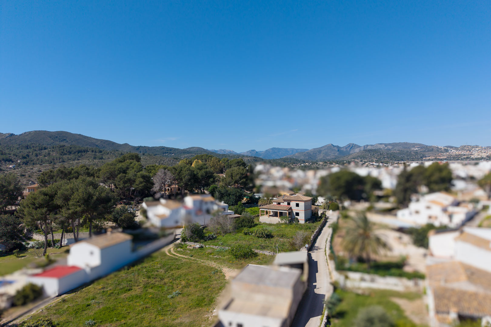 Vista aérea de la propiedad en construcción sobre una amplia parcela verde en Gata de Gorgos, con las montañas del interior al fondo bajo un cielo despejado.