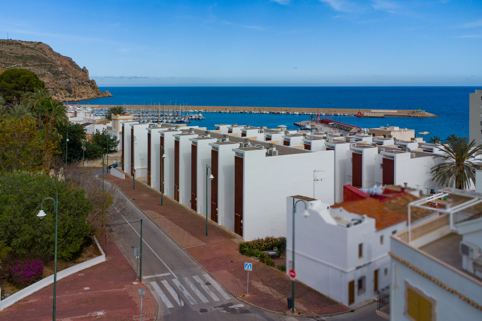 Vista panorámica del puerto de Jávea y el mar Mediterráneo, mostrando la arquitectura blanca moderna, calles peatonales y el entorno costero bajo un cielo despejado.