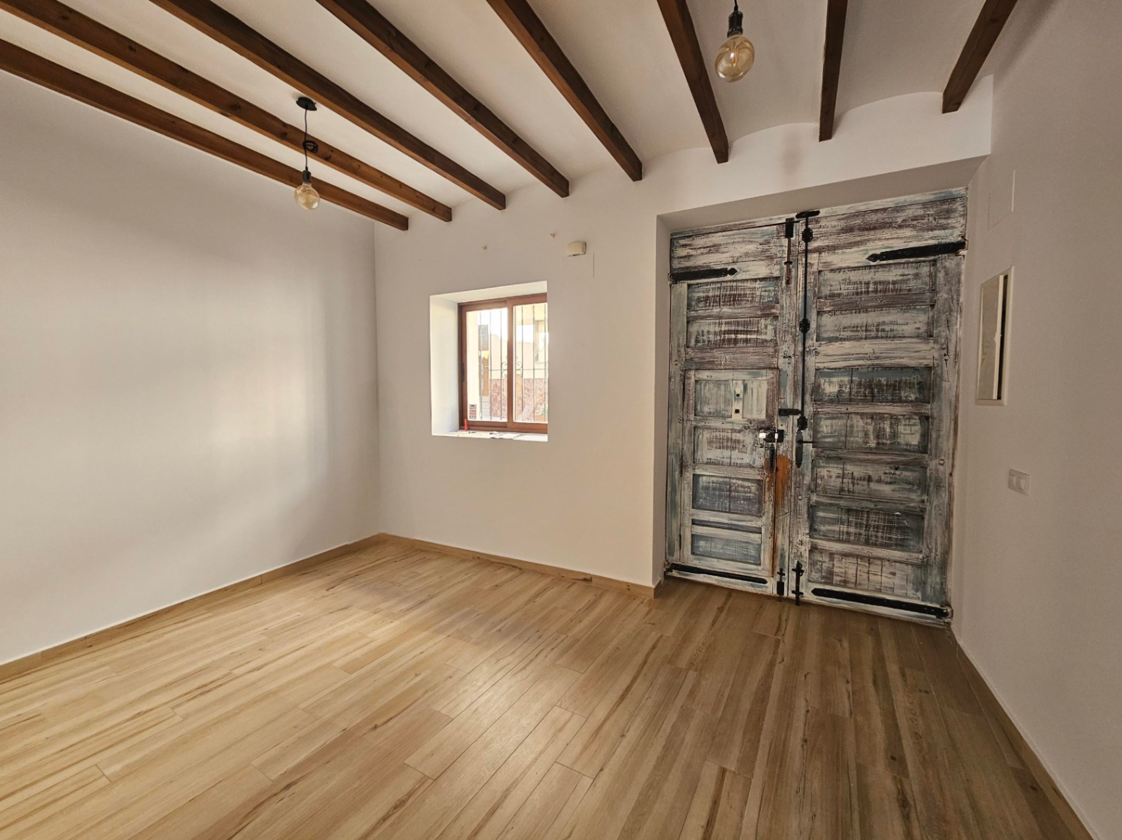 Entrada con vigas de madera vista, suelos de gres efecto madera y una gran puerta rústica restaurada con herrajes de hierro originales.