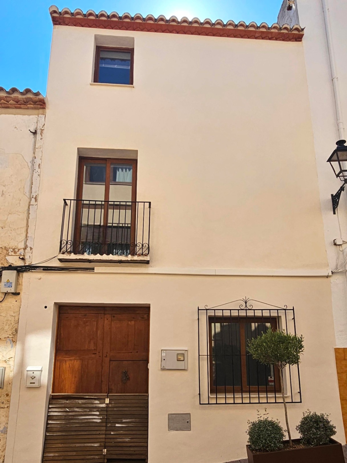 Fachada de casa de pueblo de tres plantas con puerta de madera, balcón de forja en el primer nivel y ventanas con marcos de madera y rejería tradicional.