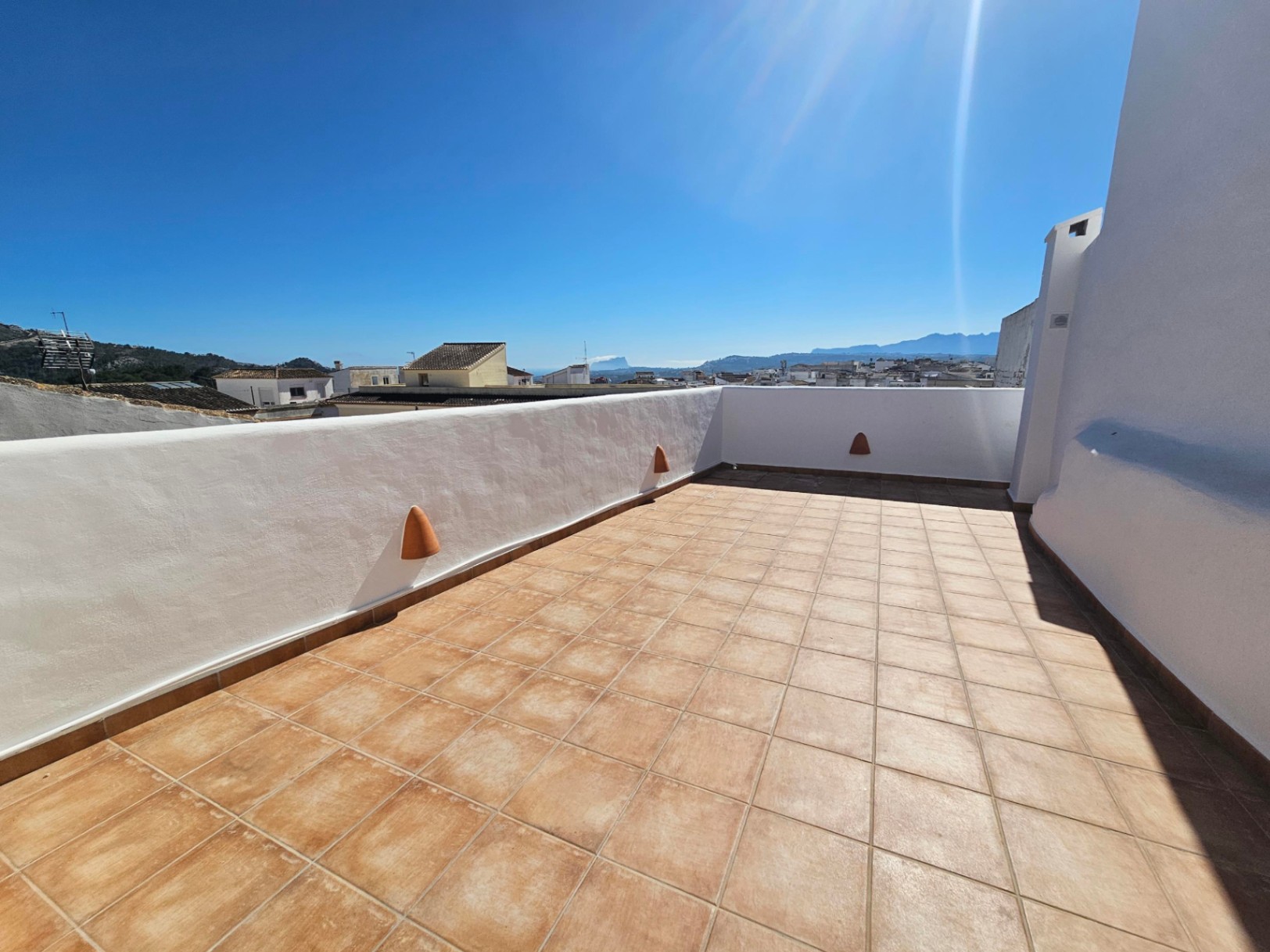 Terraza superior con suelo de baldosas cerámicas, muros encalados y vistas panorámicas al pueblo, el valle y el Peñón de Ifach bajo el sol.