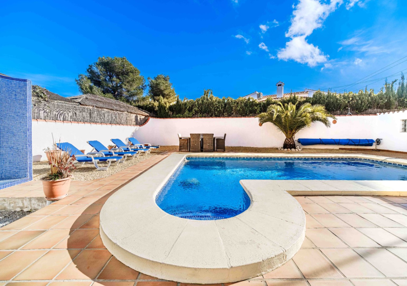 Piscina de agua salada con escalera romana, rodeada de una terraza de gres y zona de tumbonas sobre grava, junto a un comedor exterior y palmera.