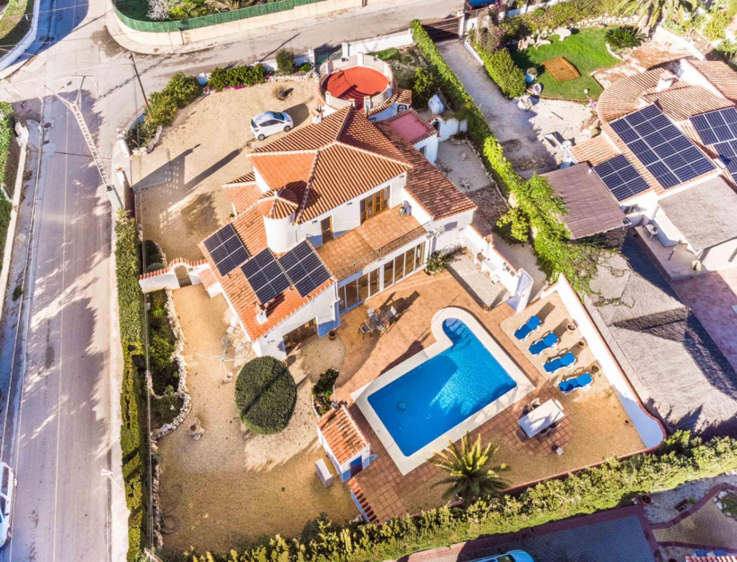 Vista aérea de la villa que muestra la piscina privada, el solárium con tumbonas, la instalación de paneles solares en el tejado y la amplia parcela en esquina.