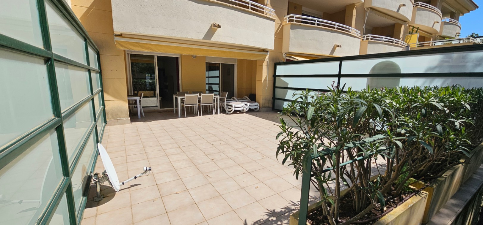 Amplia terraza privada en planta baja con suelo cerámico, zona de comedor exterior, tumbonas y paneles de cristal translúcido para mayor privacidad.