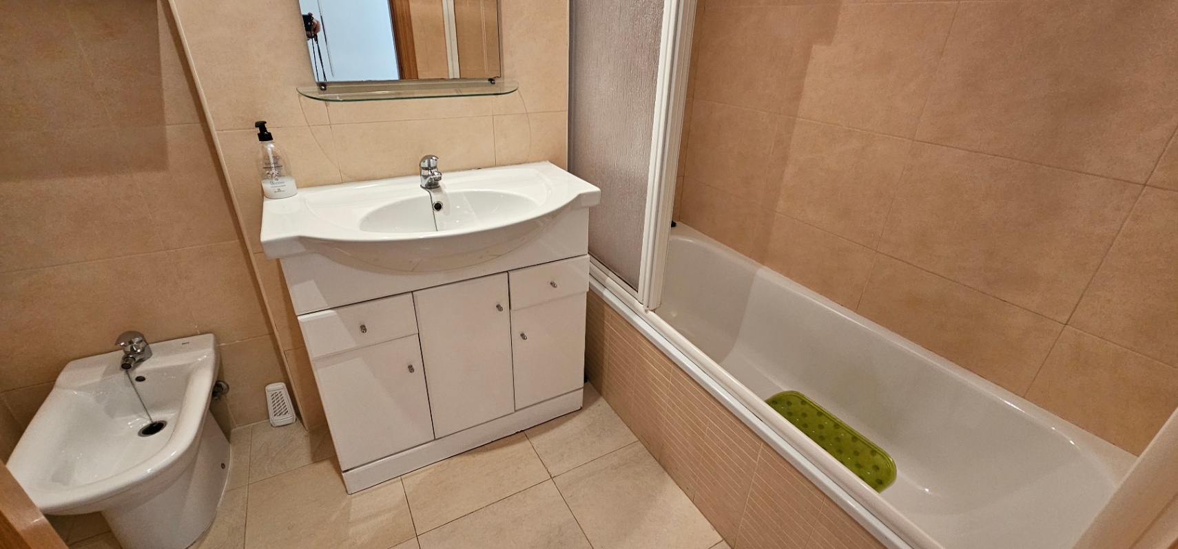 Cuarto de baño con azulejos en tonos crema, equipado con bañera, bidet y un mueble lavabo blanco con almacenamiento integrado.