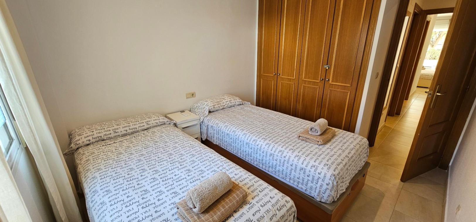 Dormitorio con dos camas individuales, un amplio armario empotrado de madera con cuatro puertas y suelos de gres cerámico en tonos claros.