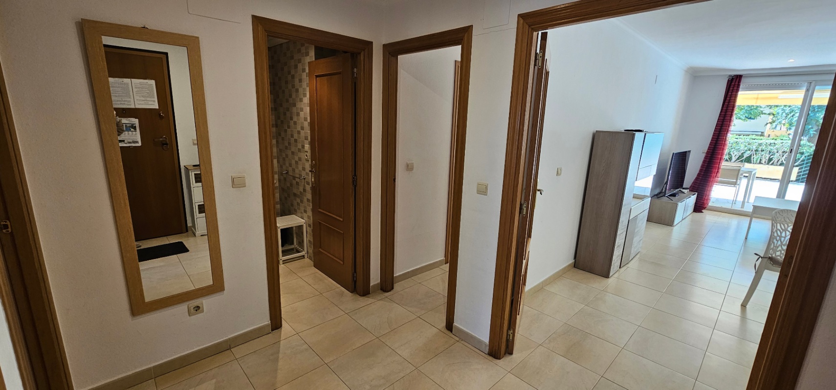 Pasillo distribuidor con suelos cerámicos y carpintería de madera, que conecta el salón-comedor con un baño de mosaico gris y los dormitorios.