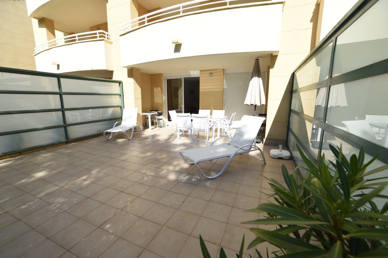 Terraza privada con suelo cerámico, equipada con tumbonas blancas y zona de comedor exterior bajo porche, delimitada por paneles de privacidad.