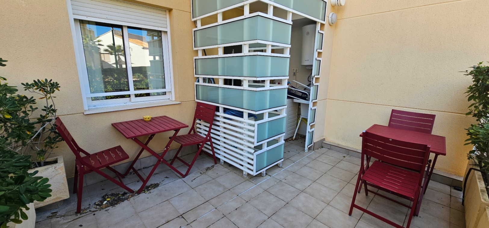Terraza privada con suelo de gres, mobiliario exterior en color granate y un cerramiento funcional de lamas blancas y cristal traslúcido para la zona de lavadero.